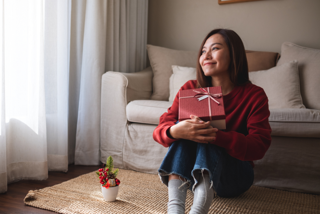 A woman sitting on the floor, smiling, and holding a gift box.