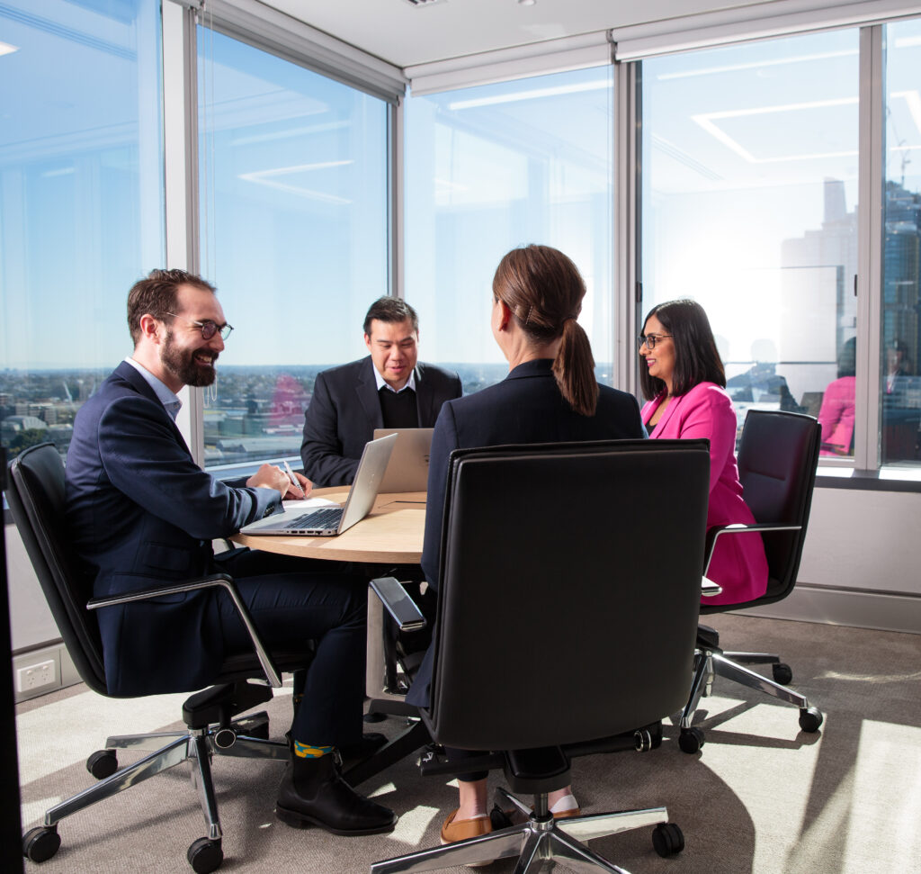 four people in meeting room at round table working and smiling