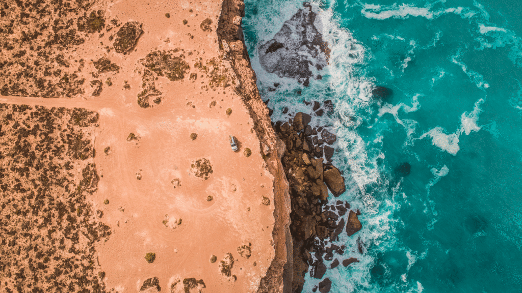 Aerial view of dark sandy coust with rocks and rough sea